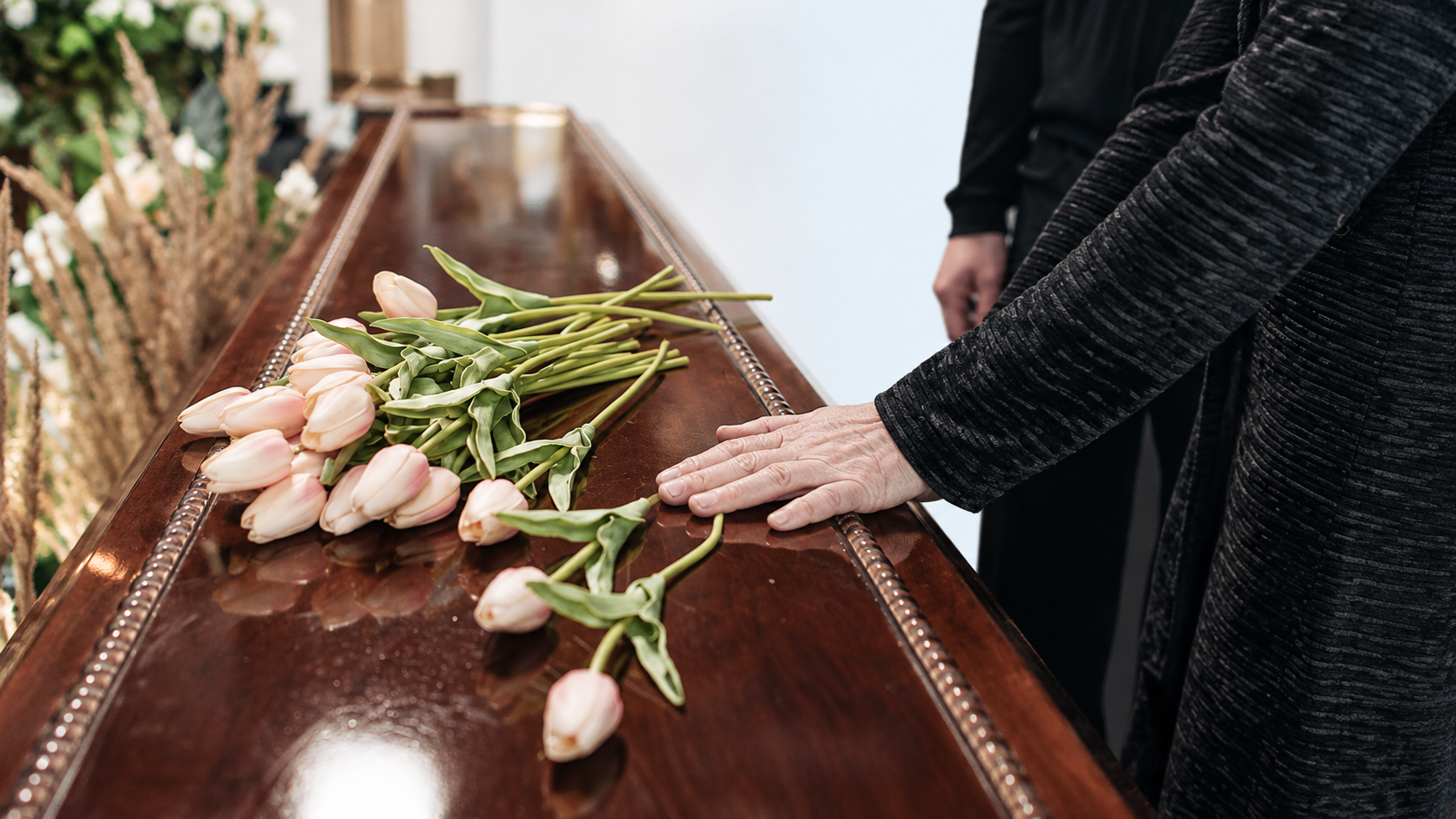 Family member placing flowers on a wooden casket during a funeral farewell